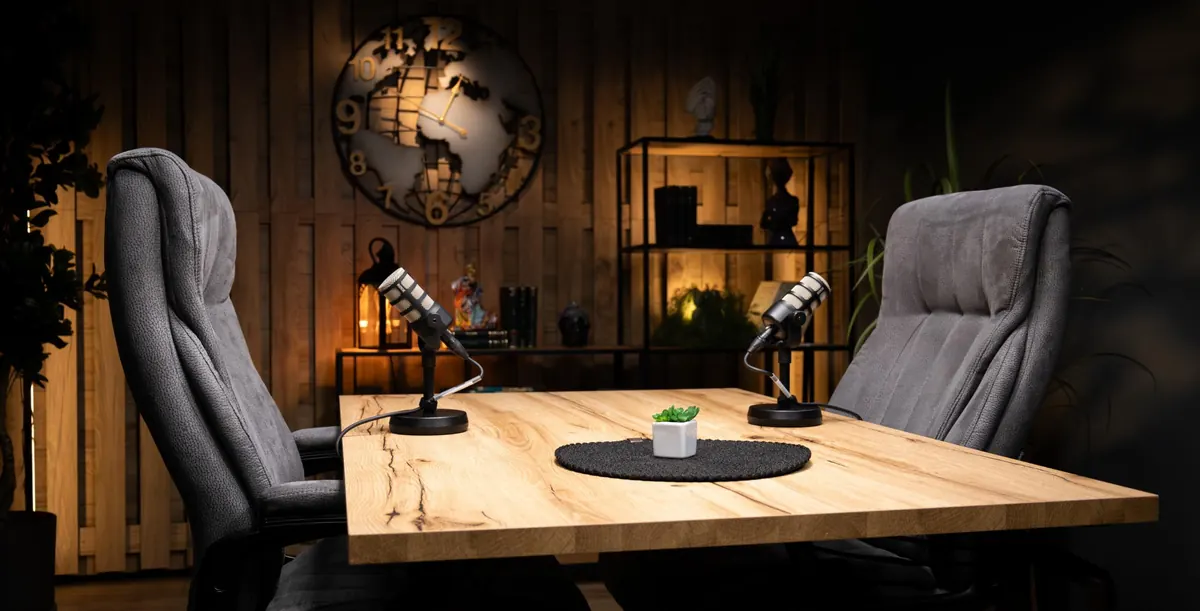 Studio podcast BUG52 din București — masă din lemn cu două microfoane profesionale și fotolii grise pregătite pentru filmare video podcast